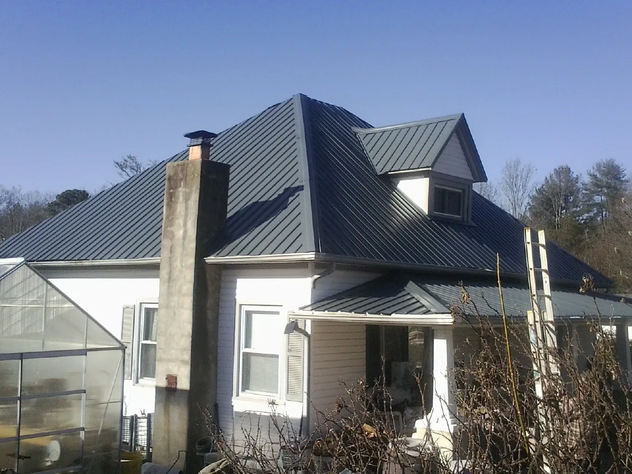 Dark blue standing seam metal roof on a white farmhouse with dormer — Slate & Tile Roof Repair by Roofing Brothers in Niagara