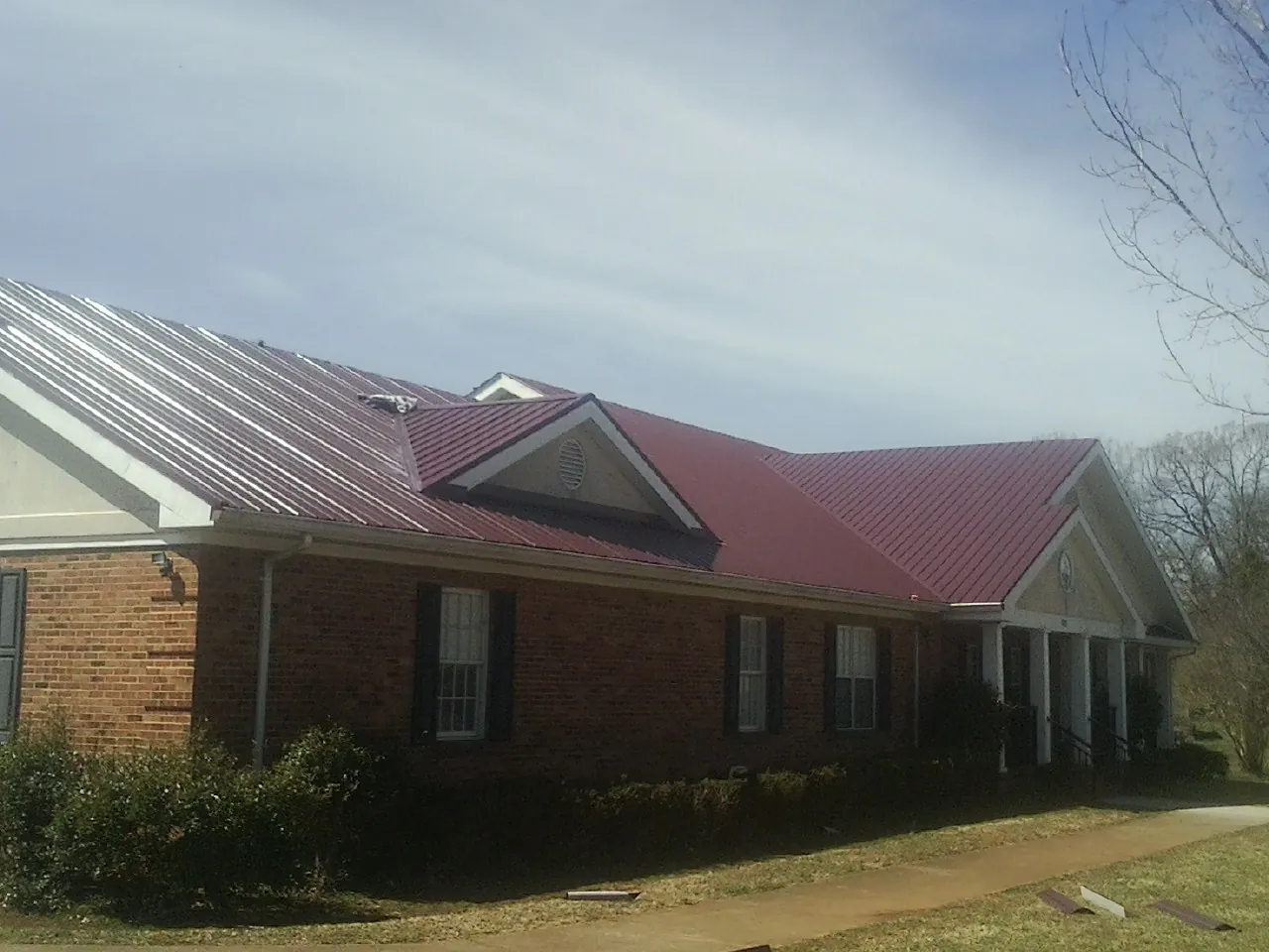 Red metal roof with gabled entries on a long brick building, from a Hail Damage Roof Repair job in Niagara