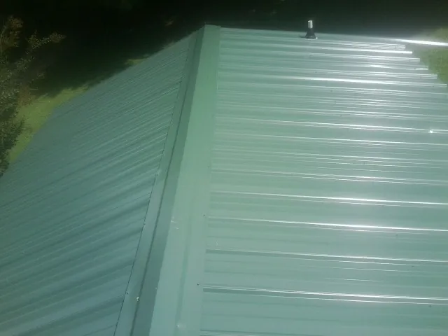 New green metal panels meeting at the ridge of a roof — Flat Roof Repair work by our crew in Niagara