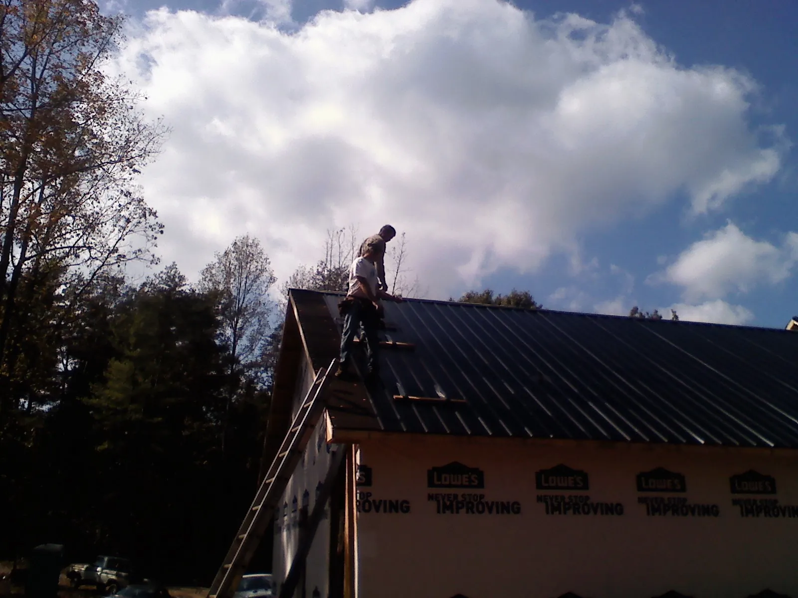 Roofer fastening dark metal panels high against a cloudy sky, from a Roof Inspection job in Niagara