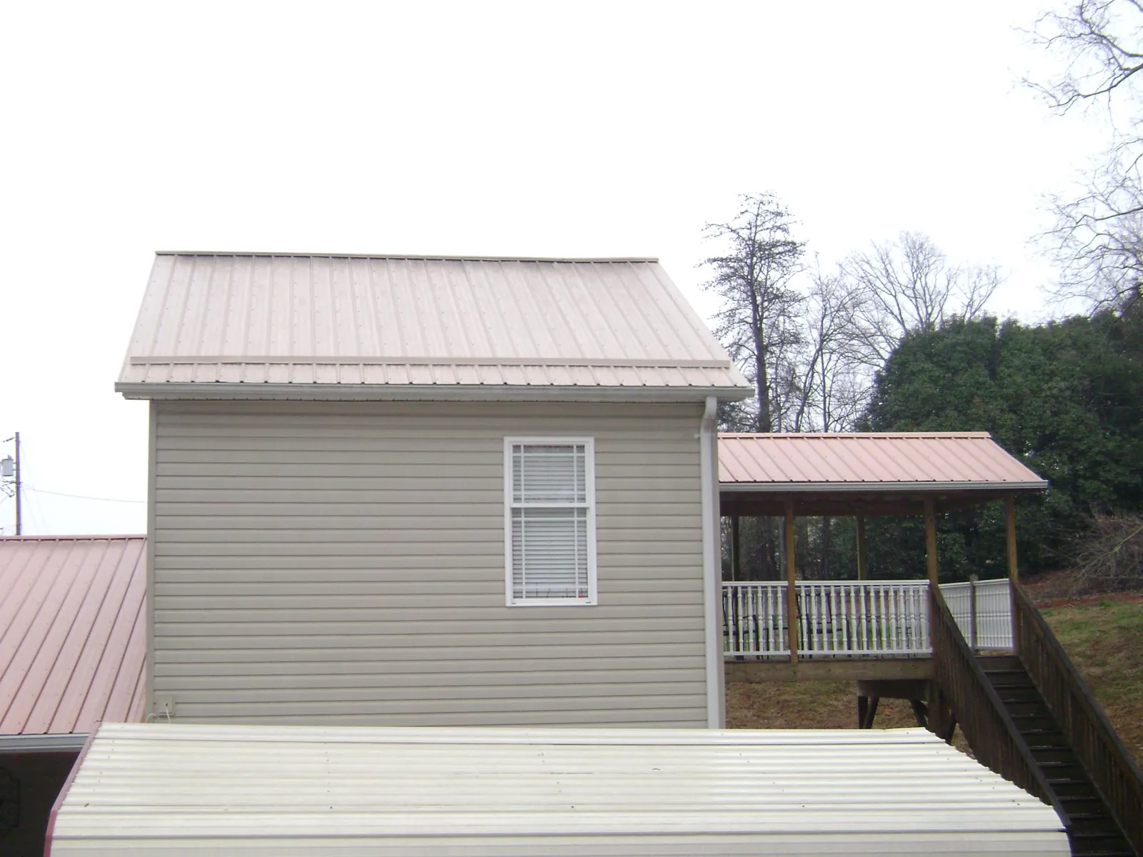 Tan metal roofs on a two story addition and attached porch, from a Roof Replacement job in Niagara